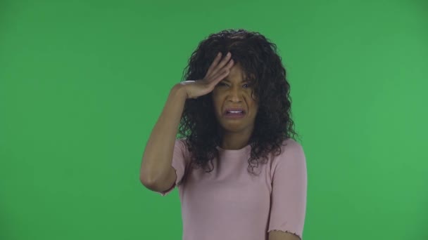 Retrato de hermosa mujer joven afroamericana está molesto y haciendo facepalm. Morena ardiente con el pelo ondulado en jeans y una blusa beige en una pantalla verde en el estudio. — Vídeo de stock