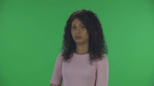Portret pięknej afrykańskiej młodej kobiety spogląda w kamerę z niechęcią. Płonąca brunetka z falowanymi włosami w dżinsach i beżową bluzką na zielonym ekranie w studio. — Wideo stockowe