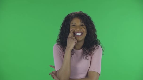 Güzel Afrikalı Amerikalı genç bir kadının portresi hayal kuruyor ve gülümsüyor. Yanan esmer, kot pantolonlu dalgalı saçlı ve stüdyoda yeşil ekranda bej bir bluz.. — Stok video