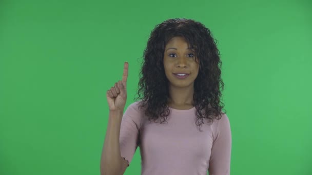 Portret pięknej afrykańskiej młodej kobiety spogląda w kamerę i pokazuje pięść, a następnie liczy jeden, dwa, trzy, cztery, pięć palców. Płonąca brunetka z falowanymi włosami w dżinsach i beżową bluzką — Wideo stockowe