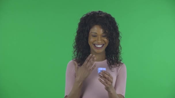 Портрет красивої афроамериканської молодої жінки дивиться на камеру і відкриває невелику коробку з несподіванкою і засмучується. Палаюча брюнетка з хвилястим волоссям в джинсах і бежева блузка на зеленому — стокове відео
