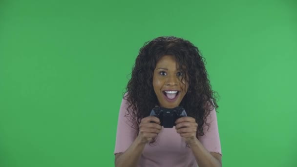 Portret pięknej afrykańskiej młodej kobiety patrzy w kamerę i gra w gry wideo za pomocą bezprzewodowego kontrolera z radością i wow emocji. Płonąca brunetka z falowanymi włosami w dżinsach i — Wideo stockowe