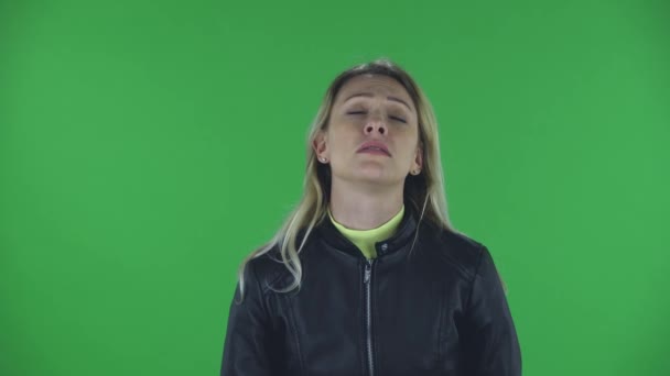 Portrait of beautiful young woman is looking straight . She has temperature is coughs and covers itself with an elbow. Blonde with loose hair in a black jacket and jeans on a green screen in the — Stock Video