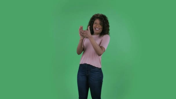 美しいアフリカ系アメリカ人の若い女性の肖像画は、カメラを見て、不満を抱いて手をたたいています。燃えるブルネットとともに波状の髪でジーンズとベージュのブラウスで緑の画面に — ストック動画