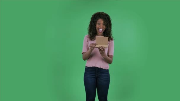 Портрет красивой африканской молодой женщины-американки смотрит в камеру и открывает подарок с большим удивлением и удивлением и радостью. Горящая брюнетка с волнистыми волосами в джинсах и бежевым — стоковое видео