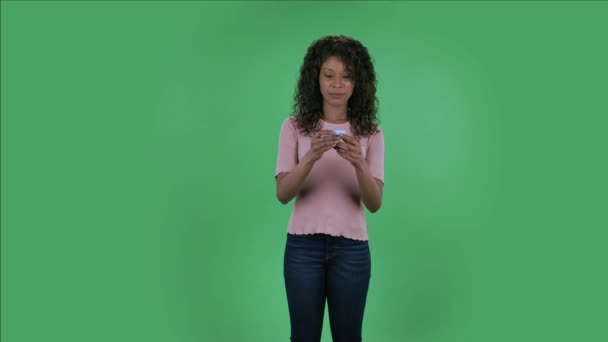 美しいアフリカ系アメリカ人の若い女性の肖像画は、カメラを見て、驚きと小さな箱を開けて動揺しています。燃えるブルネットとともに波状の髪でジーンズとベージュのブラウスで緑 — ストック動画