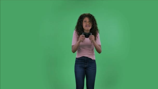 Portrait of beautiful african american young woman is looking at camera and playing a video game using a wireless controller with joy and wow emotions. Burning brunette with wavy hair in jeans and a — Stok Video