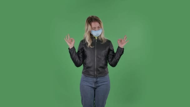 Portret van mooie jonge vrouw in medische beschermende gezichtsmasker is kijken naar camera is ontspannen en mediteren. Blond met los haar in een zwart jasje en jeans op een groen scherm in de studio — Stockvideo