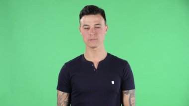 Yakışıklı bir gencin portresi. Gülümsüyor, kalp hareketi yapıyor ve hava öpücüğü veriyor. Yeşil Ekran.