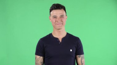 Yakışıklı bir gencin portresi. Gülümsüyor, kalp hareketi yapıyor ve hava öpücüğü veriyor. Yeşil Ekran.