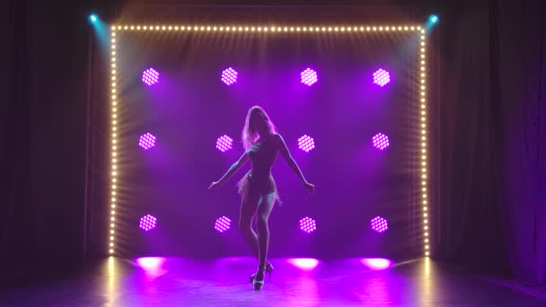 Молода сексуальна жінка йде танцювати запальні танці в темній студії. Силует жіночого тіла на тлі яскравих неонових вогнів. Повільний рух . — стокове відео