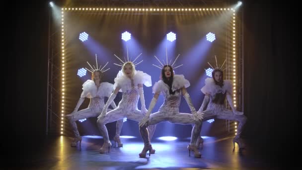 Danse chorégraphique moderne exécutée par un groupe de jeunes femmes élancées en salopette à volants serrés et couronnes. Tourné dans un studio sombre avec des néons en arrière-plan. Mouvement lent. — Video