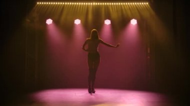 Baştan çıkarıcı kısa şortu ve bluzu olan genç ve güzel bir bayanın silueti sahne ışıkları altında baştan çıkarıcı bir şekilde dans ediyor. Git dans et, yaşam tarzı, kendine güven, eğlence. Yavaş çekim.