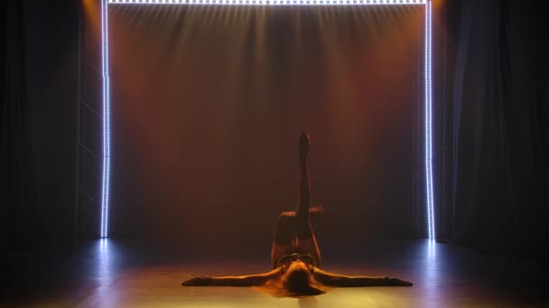 Jovem morena caucasiana apaixonada dançando cativantemente em lingerie feminina preta em um estúdio escuro com luz encenada. Silhueta de um corpo tonificado esbelto, movimento lento. — Vídeo de Stock