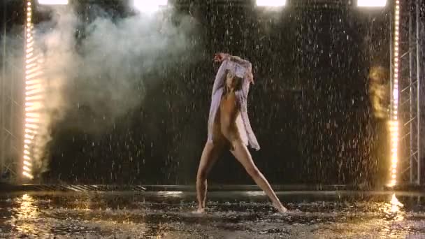 Una mujer con una camisa blanca está bailando en el escenario los bailes dramáticos del ballet moderno bajo la lluvia. Un bailarín de ballet mueve el plástico realizando una coreografía moderna en humo. Movimiento lento. — Vídeos de Stock