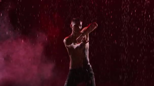 Чувственный современный балетный танец в исполнении молодого человека с татуировкой дракона под дождем. Мокрый танцор выполняет вращения с помощью прожекторов и дыма на тёмном фоне. Медленное движение. Закрыть. — стоковое видео