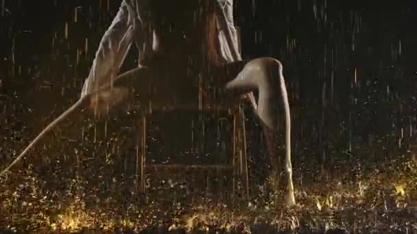 Une jeune femme à moitié nue en maillot de bain beige et chemise effectue des mouvements en douceur avec ses jambes alors qu'elle est assise sur une chaise. Ballerine de danse contemporaine posant sous la pluie battante. Au ralenti. Gros plan. — Video