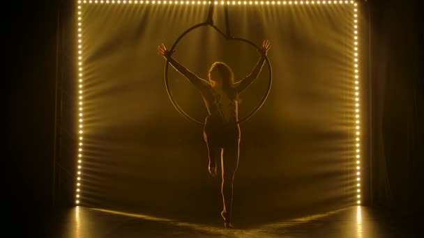 Antenni akrobaatti kehässä. Nuori nainen suorittaa akrobaattisia elementtejä ilmassa rengas ympäröi pehmeä keltainen valo. Hidastus. — kuvapankkivideo