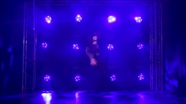 Kadın akrobatik elementler sergiliyor ve mavi neon ışıkların arka planında asılı duran bir halkada dönüyor. Yavaş çekim.