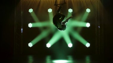 Siluet kadın sirk sanatçısı esnekliğini bir hava çemberinde gösteriyor. Yeşil ışıkları olan karanlık bir stüdyoda akrobatik hareketlerin zarif performansı. Yavaş çekim.