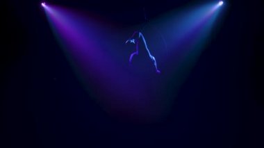 Hava halkası üzerinde kadın bir akrobat tarafından yapılan sicim ve denge elementleri. Spot ışıkları altında siluetler. Yavaş çekim.