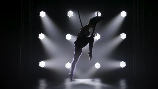 Frumoasa gimnastă aeriană creț efectuează elemente pe cerc aerian. Silueta grațioasă a unei tinere fete în lumina reflectoarelor se ridică din întuneric. Slow motion . — Videoclip de stoc