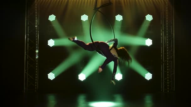 Une artiste de cirque démontre sa flexibilité dans un cercle aérien. Performance gracieuse de cascades acrobatiques dans un studio sombre avec des feux verts. Mouvement lent. — Video