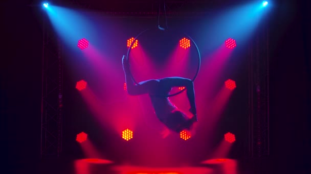 Air gymnastika žena provádí akrobacii triky na letecké obruče. Žena dělá nějaké akrobatické prvky na vzduchovém obručí uvnitř. Silueta. Zpomalený pohyb. — Stock video