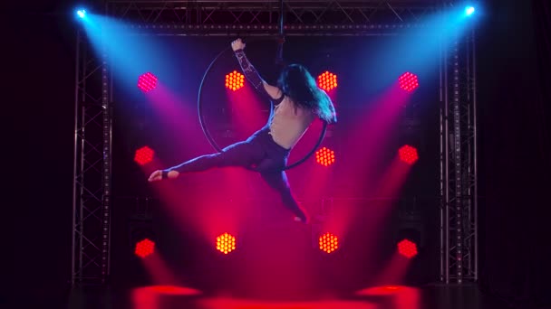 Air gymnastique femme effectue des tours d'acrobatie sur cerceau aérien. Femme faisant quelques éléments acrobatiques sur cerceau aérien à l'intérieur. Spectacle acrobatique dans un studio sombre avec éclairage de scène rouge. Mouvement lent. — Video