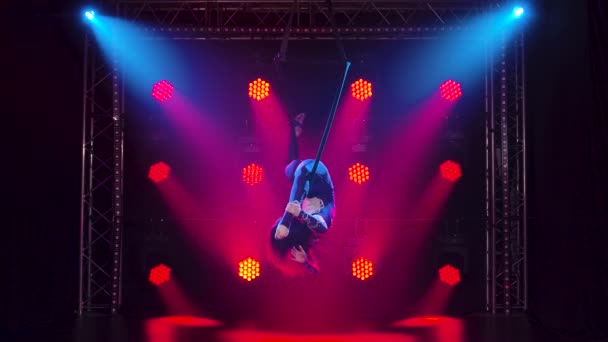 Воздушная гимнастка выполняет акробатические трюки на воздушном обруче. Женщина делает несколько акробатических элементов на воздушном обруче в помещении. Акробатическое шоу в темной студии с красной подсветкой сцены. Медленное движение. — стоковое видео