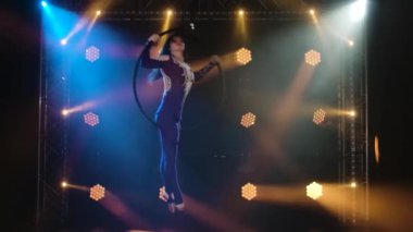 Genç hava sanatçısı kadın bir hava çemberinde hızla dönüyor. Dinamik neon ışıkları olan karanlık bir stüdyoda çekildi. Yavaş çekim.