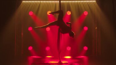 Profesyonel bir akrobat, havadaki ipeğin yardımıyla havada dönüyor. İnce, kırmızı neon ışıklı genç bir kadının siluetleri. Yavaş çekim.