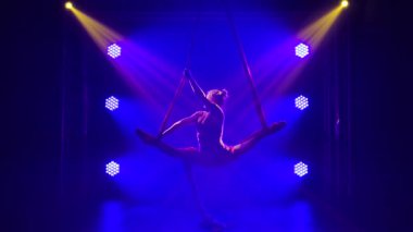 Genç ve yetenekli bir sirk kadın sanatçısı hava ipeği üzerinde denge kuruyor. Mavi ışıklı, karanlık bir stüdyoda akrobatik bir ayakkabı. Yavaş çekim.