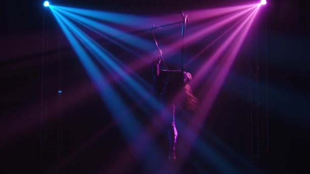 Young adult woman using aerial hoop, making flexibility twine exercise in air. An aerialist is silhouetted in dynamic beautiful neon lights. Slow motion. — Stock Video