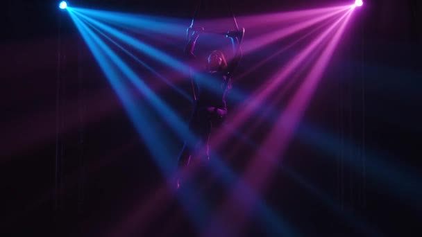 Young adult woman using aerial hoop, making flexibility twine exercise in air. An aerialist is silhouetted in dynamic beautiful neon lights. Slow motion. — Stock Video