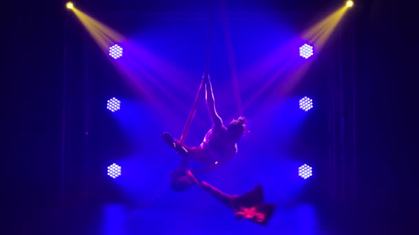 Une jeune artiste de cirque talentueuse effectue un équilibrage sur la soie aérienne. Chaussure acrobatique dans un studio sombre avec néons bleus. Mouvement lent. — Video