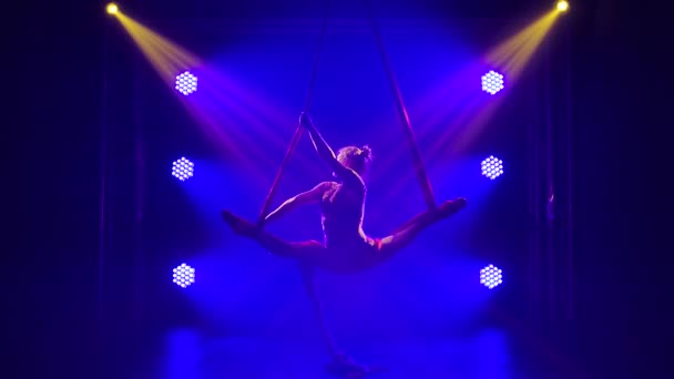Una joven talentosa intérprete de circo realiza un equilibrio en la seda aérea. Zapato acrobático en un estudio oscuro con luces de neón azul. Movimiento lento. — Vídeos de Stock