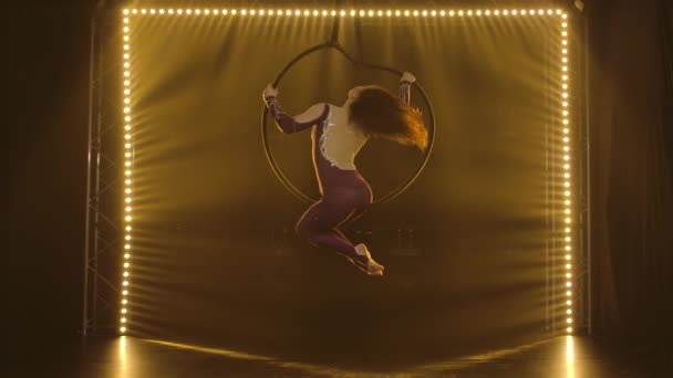 Aerial acrobat in the ring. A young woman performs the acrobatic elements in the air ring surrounded by soft yellow light. — Stock Video