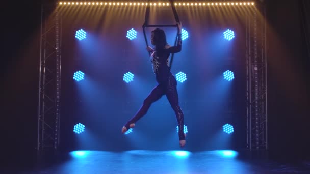 Sziluett nő aerialista végez akrobatikus elemek és forog lógó légi karika háttér kék neon fények. — Stock videók