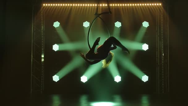 Silhouette femme artiste de cirque démontre sa flexibilité dans un cercle aérien. Performance gracieuse de cascades acrobatiques dans un studio sombre avec des feux verts. — Video