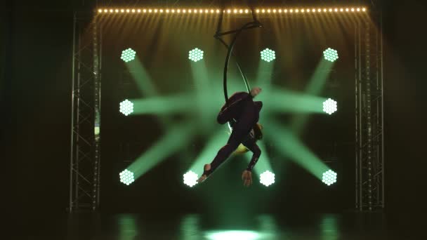 Een vrouwelijke circusartiest demonstreert haar flexibiliteit in een luchtkring. Gracieuze uitvoering van acrobatische stunts in een donkere studio met groen licht. — Stockvideo