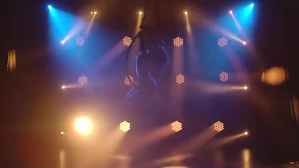 Silhouette young aerial artist woman rotates rapidly in an aerial circle. Filmed in a dark studio with dynamic neon lights. — Stock Video