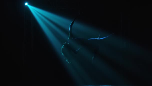 En kvinnlig flygakrobats prestation. Mot en svart bakgrund, i strålkastarna, kan en siluett av en gymnast på en luftcirkel ses. — Stockvideo