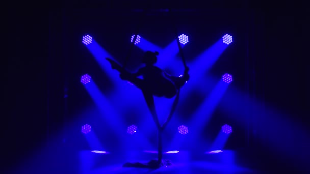 Kvinnlig antenn jämvikt gymnast utför balansering på en luft silke i en mörk studio med blå scenbelysning. Silhuett av en smal kropp. Närbild. — Stockvideo