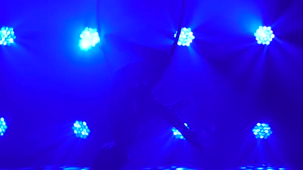 Silhouette of flexible woman hanging in an aerial acrobatics ring performs complex tricks. Aerial acrobat close up in a dark studio with blue stage lighting. — Stock Video