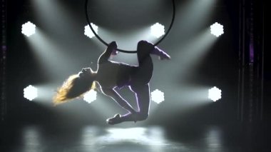 Silüet genç kadın hava halkasındaki akrobatik elementleri sergiliyor. Spot ışığında karanlık bir stüdyoda çekildi. Kapat..