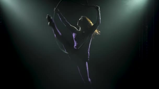 Professional aerial gymnast female rotates on an air hoop. Silhouette of an attractive woman in the rays of studio light on a black background. Close up. — Stock Video