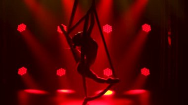 Profesyonel bir akrobat, havadaki ipeğin yardımıyla havada dönüyor. İnce, kırmızı neon ışıklı genç bir kadının siluetleri. Kapat..