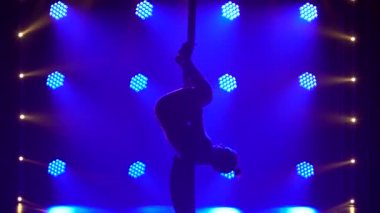 Genç bir kadın hava ipeği üzerinde sicim çalışması yapıyor. Mavi ışıkta ince, esnek bir siluet. Kapat..