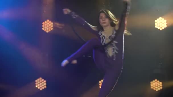 En akrobatisk show på en luftslinga framförd av en ung attraktiv cirkusartist. Utförande i en mörk studio med neonljus. Närbild. — Stockvideo